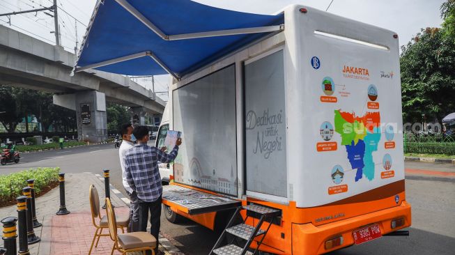 Petugas Dinas Pariwisata dan Ekonomi Kreatif DKI Jakarta menjelaskan tentang destinasi wisata kepada warga saat uji coba Tourist Information Center Mobile (TICM) di Terminal Blok M, Jakarta Selatan, Jumat (12/3/2021). [Suara.com/Alfian Winanto]
