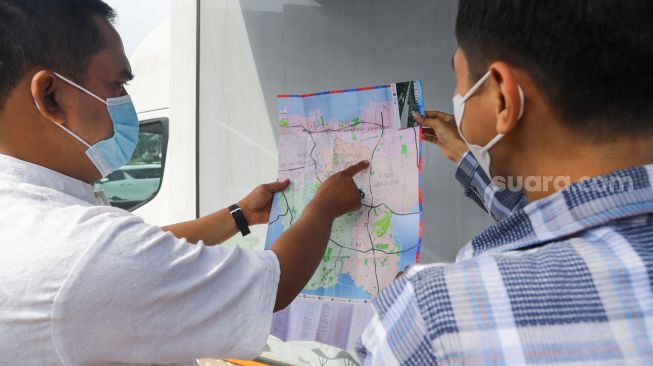 Petugas Dinas Pariwisata dan Ekonomi Kreatif DKI Jakarta menjelaskan tentang destinasi wisata dengan menggunakan peta kepada warga saat uji coba Tourist Information Center Mobile (TICM) di Terminal Blok M, Jakarta Selatan, Jumat (12/3/2021). [Suara.com/Alfian Winanto]