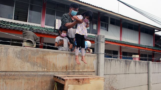 Asep (29) salah seorang penghuni rumah mengangkat anaknya melewati tembok untuk bermain dari dalam rumahnya yang terkepung tembok beton di Tajur Ciledug, Tangerang, Banten, Senin (15/3/2021). ANTARA FOTO/Muhammad Iqbal