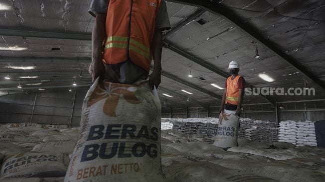 Pekerja menata karung berisi beras di Gudang Bulog Kanwil DKI dan Banten, Kelapa Gading, Jakarta, Kamis (18/3/2021). [Suara.com/Angga Budhiyanto]