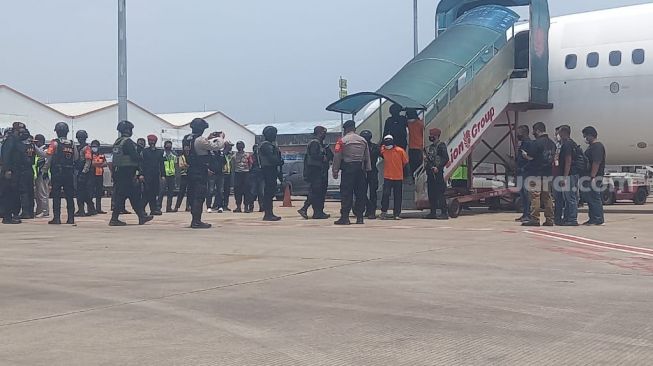 Para terduga teroris Jatim turun dari pesawat dengan kondisi kaki dirantai dan mata ditutup saat tiba di Landasan Apron Terminal Kargo Bandara Soekarno-Hatta (Soetta), Tangerang, Kamis (18/3/2021). [Suara.com/Muhammad Jehan Nurhakim]