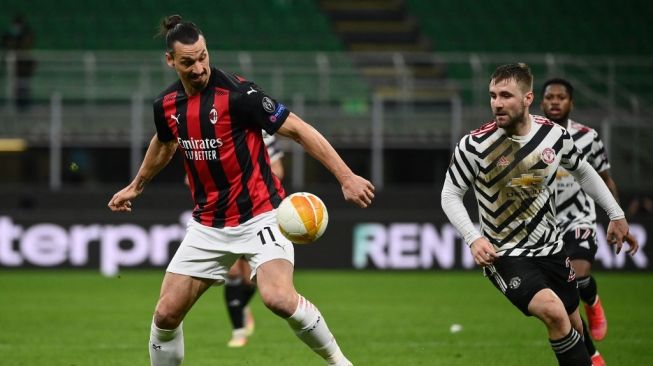 Bek sayap Manchester United, Luke Shaw coba merebut bola dari penyerang AC Milan, Zlatan Ibrahimovic dalam pertandingan leg kedua babak 16 besar Liga Europa (Milan vs MU) di San Siro, Jumat (19/3/2021) dini hari WIB. [Marco BERTORELLO / AFP].