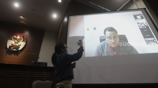 Seorang jurnalis mengambil gambar Mantan Menteri Sosial Juliari Peter Batubara saat memberikan kesaksian dalam sidang yang berlangsung secara virtual di Gedung KPK, Jakarta, Senin (22/3/2021). [Suara.com/Angga Budhiyanto]