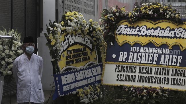 Salah seorang kerabat berdiri di dekat karangan bunga tanda berduka cita atas meninggalnya Mantan Jaksa Agung Basrief Arief di rumah duka di kawasan Petogogan, Kebayoran Baru, Jakarta, Selasa (23/3/2021). [Suara.com/Angga Budhiyanto]