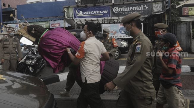 Petugas Suku Dinas Sosial dan Satpol PP Jakarta Selatan membawa pengamen ondel-ondel yang terjaring razia Penyandang Masalah Kesejahteraan Sosial (PMKS) di kawasan Bulungan, Jakarta , Rabu (24/3/2021). [Suara.com/Angga Budhiyanto]