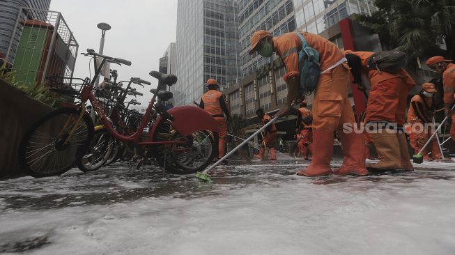 Petugas gabungan Unit Kerja Perangkat Daerah (UKPD) membersihkan trotoar sepanjang Jalan Sudirman-Thamrin, Jakarta, Sabtu (27/3/2021). [Suara.com/Angga Budhiyanto]