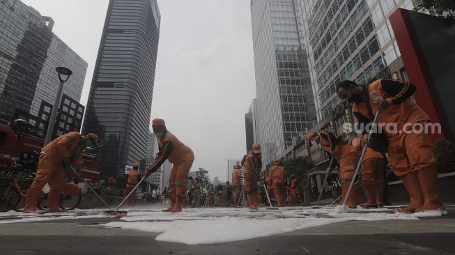 Petugas gabungan Unit Kerja Perangkat Daerah (UKPD) membersihkan trotoar sepanjang Jalan Sudirman-Thamrin, Jakarta, Sabtu (27/3/2021). [Suara.com/Angga Budhiyanto]