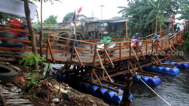 Seorang pejalan dan pengendara sepeda motor melintasi Jembatan alternatif, Tambun Selatan, Kabupaten Bekasi (30/03/21). [Suara.com/Dian Latifah]