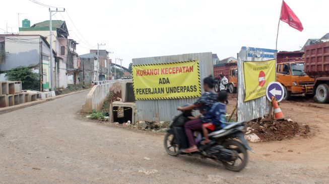 Pengendara melewati jalur perlintasan kereta api yang berada di samping proyek Underpass Cibitung, Kecamatan Cibitung, Kabupaten Bekasi, Rabu (31/03/21). [Suara.com/Dian Latifah]