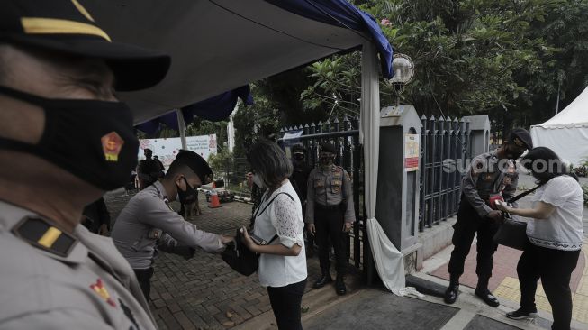 Personel kepolisian memeriksa barang bawaan jemaat yang akan memasuki Gereja Katedral, Jakarta, Kamis (1/4/2021). [Suara.com/Angga Budhiyanto]