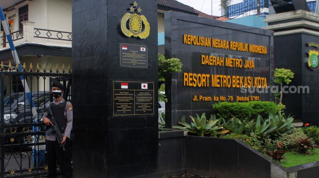 Petugas memegang laras panjang berjaga di depan pintu gerbang masuk Polres Metro Bekasi Kota, Kota Bekasi, Kamis (01/04/21). [Suara.com/Dian Latifah]    