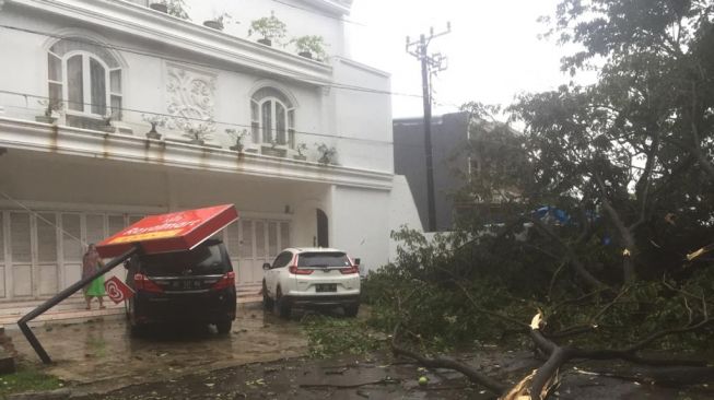 Hujan badai melanda Sulawesi Selatan menyebabkan pohon dan papan reklame tumbang menimpa kendaraan, Jumat 2 April 2021 / [SuaraSulsel.id / Istimewa]