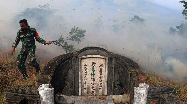 Warga menghindari asap usai mencoba memadamkan api yang membakar areal sekitar kuburan Cina saat pelaksanaan tradisi ceng beng (ziarah kubur) di Jambi, Minggu (4/4/2021). ANTARA FOTO/Wahdi Septiawan
