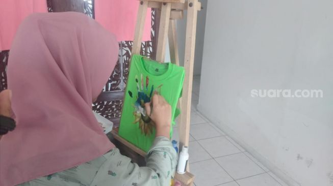 Zakiah Hafiza, mahasiswa Unand sedang melukis baju pemesanan pelanggan. [Suara.com/B.Rahmat]