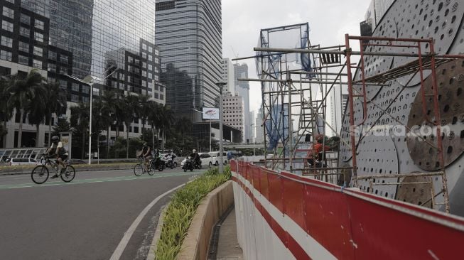 Pesepeda melintas di dekat proyek pembangunan Tugu Sepeda di Jalan Jenderal Sudirman, Jakarta, Senin (5/4/2021). [Suara.com/Angga Budhiyanto]