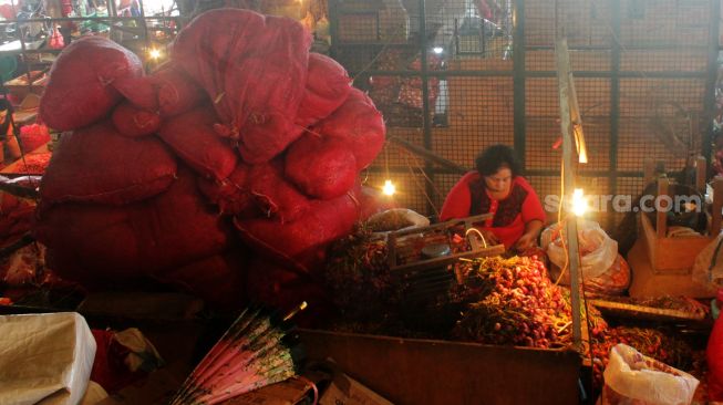 Seorang Ibu melakukan aktivitas mengupas bawang diatas kiosnya yang berda di Pasar Induk Kramat Jati, Jakarta Timur, Rabu (07/4/21). [Suara.com/Dian Latifah]  