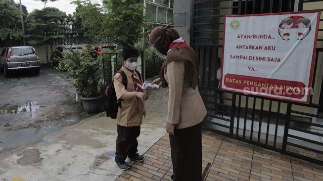 Seorang Guru mengukur suhu tubuh murid pada hari pertama uji coba pembelajaran tatap muka di SD Negeri Kenari 08 Pagi, Jakarta, Rabu (7/4/2021). [Suara.com/Angga Budhiyanto]