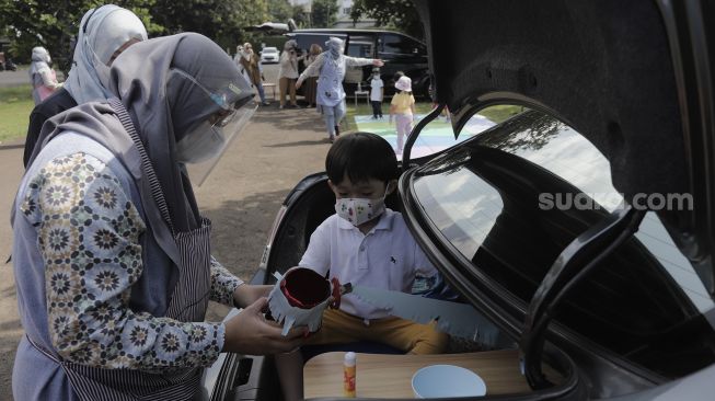 Seorang siswa taman kanak-kanak (TK) didampingi orang tuanya membuat miniatur beduk saat mengikuti proses pembelajaran secara Drive in Learning (DRIL) di area parkir Padepokan Pencak Silat Indonesia, Jakarta, Kamis (8/4/2021). [Suara.com/Angga Budhiyanto]