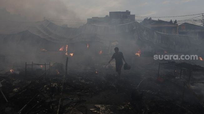 Warga berjalan di antara kepulan asap saat kebakaran melanda Pasar Lontar atau Pasar Kambing di Jalan Sabeni, Tanah Abang, Jakarta, Kamis (8/4/2021). [Suara.com/Angga Budhiyanto]