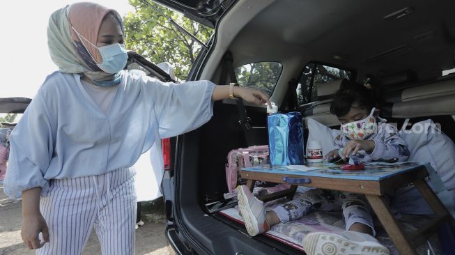 Seorang siswa taman kanak-kanak (TK) didampingi orang tuanya membuat miniatur beduk saat mengikuti proses pembelajaran secara Drive in Learning (DRIL) di area parkir Padepokan Pencak Silat Indonesia, Jakarta, Kamis (8/4/2021). [Suara.com/Angga Budhiyanto]