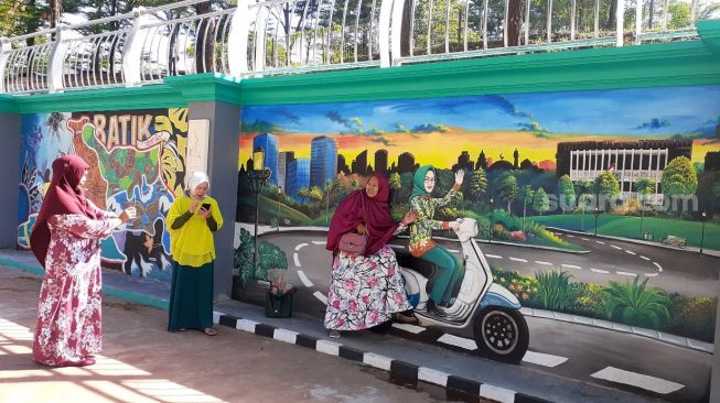 Pengunjung berfoto dengan mural Wali Kota Tangsel Airin Rachmi Diany yang mengendarai vespa di Taman Kota 2 atau Taman Jaletreng di Setu, Kota Tangerang Selatan (Tangsel), Rabu (7/4/2021). [Suara.com/Wivy Hikmatullah]