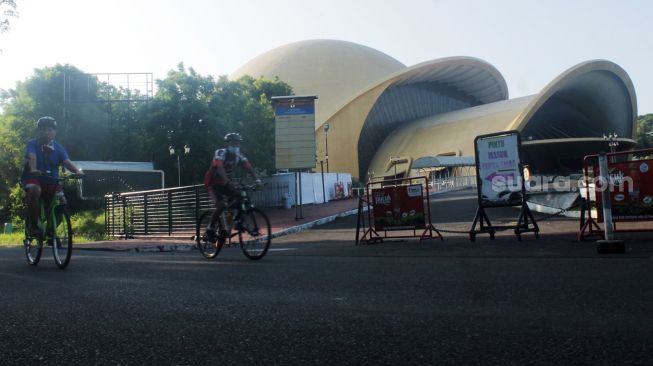 Pesepeda melewati anjungan keong mas di TMII, Jakarta Timur, Kamis (08/4/21). [Suara.com/Dian Latifah]