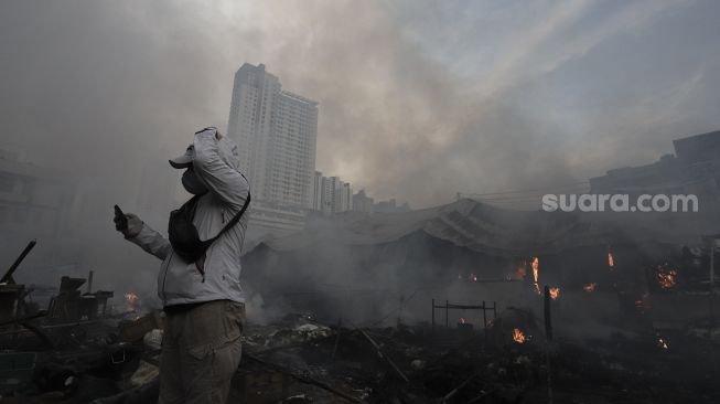 Seorang warga mengambil gambar kebakaran yang melanda Pasar Lontar atau Pasar Kambing di Jalan Sabeni, Tanah Abang, Jakarta, Kamis (8/4/2021). [Suara.com/Angga Budhiyanto]