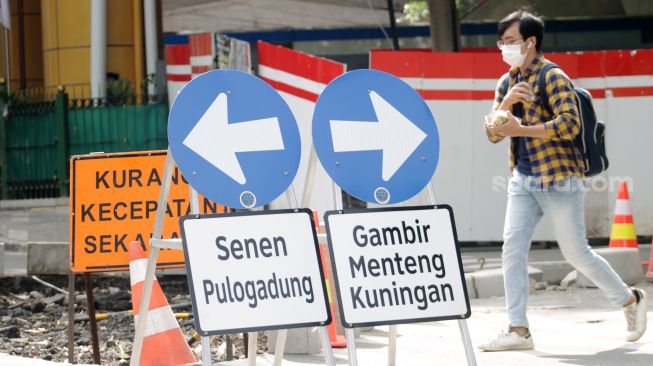 Seorang pejalan kaki melintas di dekat penunjuk jalan saat uji coba penerapan sistem satu arah di kawasan Gondangdia, Jakarta Pusat, Jumat (9/4/21). [Suara.com/Dian Latifah]  