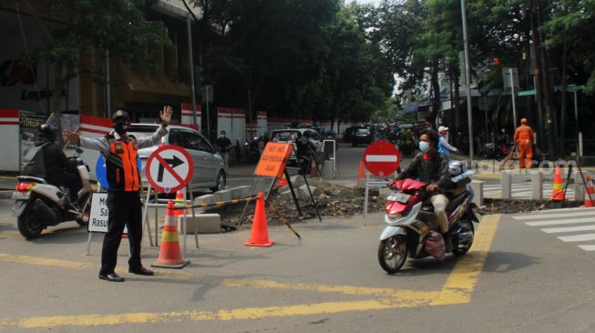 Petugas Dishub DKI Jakarta mengatur arus lalu lintas kendaraan saat uji coba penerapan sistem satu arah di kawasan Gondangdia, Jakarta Pusat, Jumat (9/4/21). [Suara.com/Dian Latifah] 