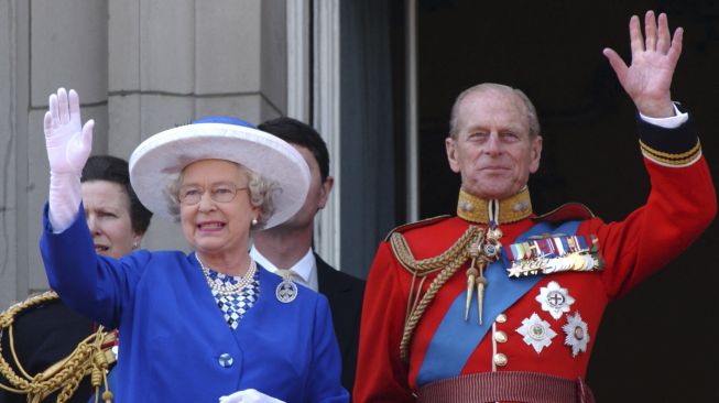 Ratu Inggris Elizabeth II (kiri) dan Duke of Edinburgh Pangeran Philip dari Inggris (kanan) melambai dari balkon Istana Buckingham di London, pada tanggal (14/6/2003). [GEOFF GARRATT / POOL / AFP]