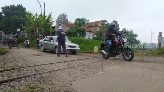 Ujang Rahmat (50 tahun) mengatur lalu lintas di perlintasan kereta api di di perlintasan Sumur Bor, Desa Cilame, Kecamatan Ngamprah, Kabupaten Bandung Barat / [SuaraJabar.id / Ferry Bangkit Rizki]