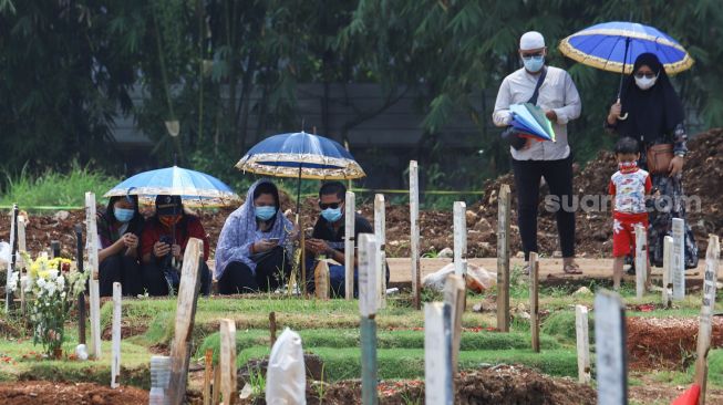 Warga berdoa diatas pusara kerabatnya saat ziarah di  area pemakaman khusus Covid - 19 TPU Bambu Apus, Jakarta Timur, Minggu (11/4/2021). [Suara.com/Alfian Winanto]