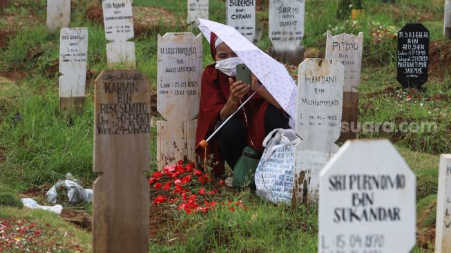 Warga berdoa diatas pusara kerabatnya saat ziarah di  area pemakaman khusus Covid - 19 TPU Bambu Apus, Jakarta Timur, Minggu (11/4/2021). [Suara.com/Alfian Winanto]