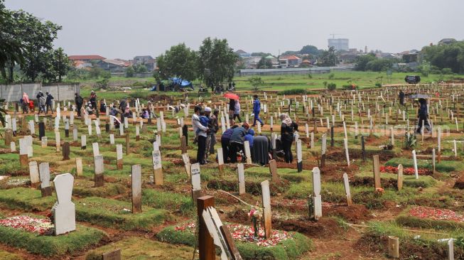 Suasana di  area pemakaman khusus Covid - 19 yang dikunjungi peziarah di TPU Bambu Apus, Jakarta Timur, Minggu (11/4/2021). [Suara.com/Alfian Winanto]