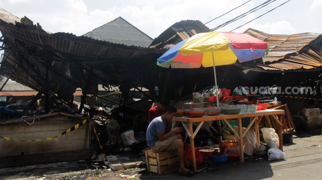 Pedagang bumbu menjajakan jualannya di depan kios yang terbakar di Jalan Sabeni Raya, Jakarta, Senin (12/4/2021). [Suara.com/Dian Latifah]