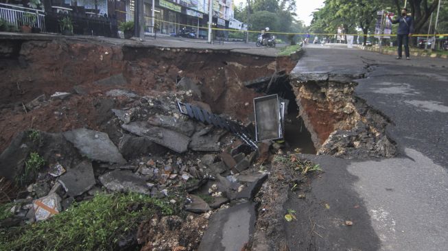 Warga memfoto jalan yang longsor di Jalan Raya Boulevard, GDC, Depok, Jawa Barat, Selasa (13/4/2021). ANTARA FOTO/Asprilla Dwi Adha

