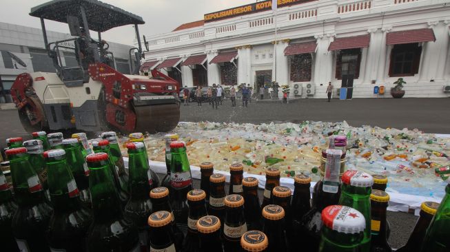 Petugas menggunakan alat berat melindas ribuan botol minuman keras, di Polrestabes Surabaya, Jawa Timur, Selasa (13/4/2021).  ANTARA FOTO/Didik Suhartono
