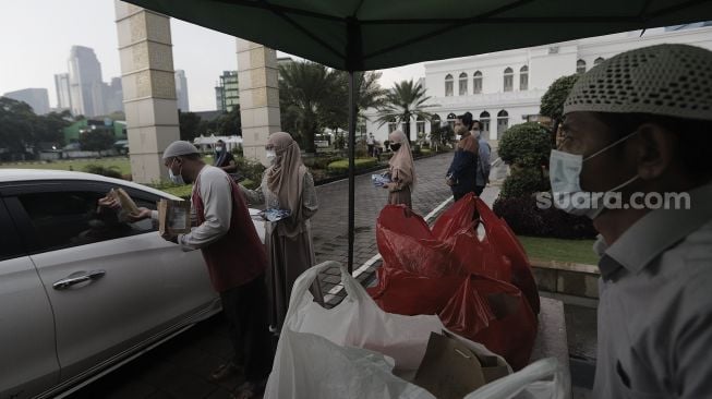 Petugas membagikan takjil kepada pengendara roda empat dengan sistem drive thru di kompleks Masjid Al-Azhar, Jakarta, Rabu (14/4/2021). [Suara.com/Angga Budhiyanto]