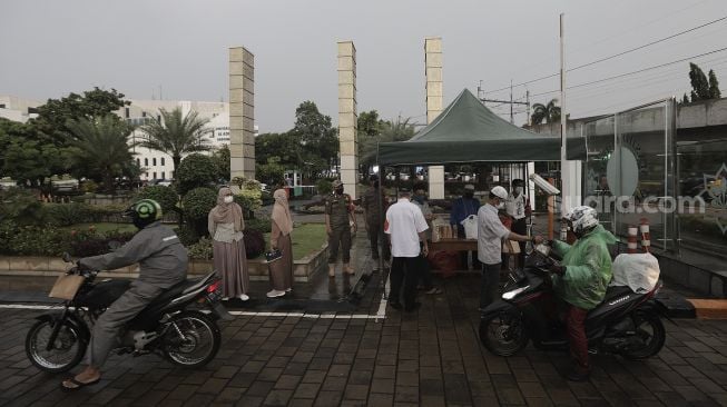 Petugas membagikan takjil kepada pengendara sepeda motor dengan sistem drive thru di kompleks Masjid Al-Azhar, Jakarta, Rabu (14/4/2021). [Suara.com/Angga Budhiyanto]