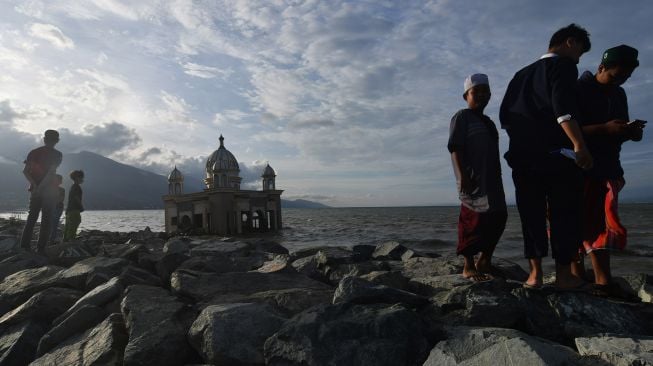 Warga menunggu datangnya waktu berbuka puasa (ngabuburit) di sekitar Masjid Terapung Arkam Babu Rahman yang rusak akibat diterjang tsunami di Pantai Teluk Palu di Palu, Sulawesi Tengah, Selasa (13/4/2021).  ANTARA FOTO/Mohamad Hamzah
