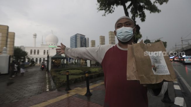 Petugas mengarahkan pengendara yang melintas untuk mengambil takjil dengan sistem drive thru di kompleks Masjid Al-Azhar, Jakarta, Rabu (14/4/2021). [Suara.com/Angga Budhiyanto]