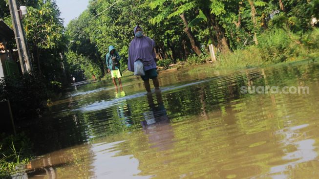 Warga menerjang banjir menggunakan sepeda motor, Perumahan Bumi Nasio Indah, Bekasi, Kamis (15/4/2021). [Suara.com/Dian Latifah]