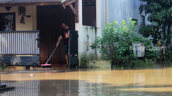 Warga membersihkan rumahnya saat air mulai surut di Perumahan Bumi Nasio Indah, Bekasi, Kamis (15/4/2021).[Suara.com/Dian Latifah]