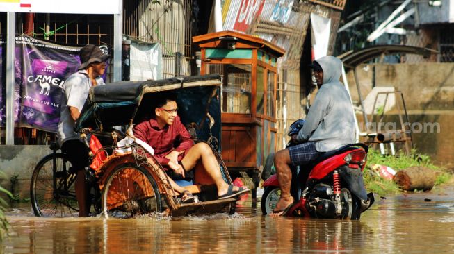 Warga melintas di genangan banjir Perumahan Bumi Nasio Indah, Bekasi, Kamis (15/4/2021). [Suara.com/Dian Latifah]