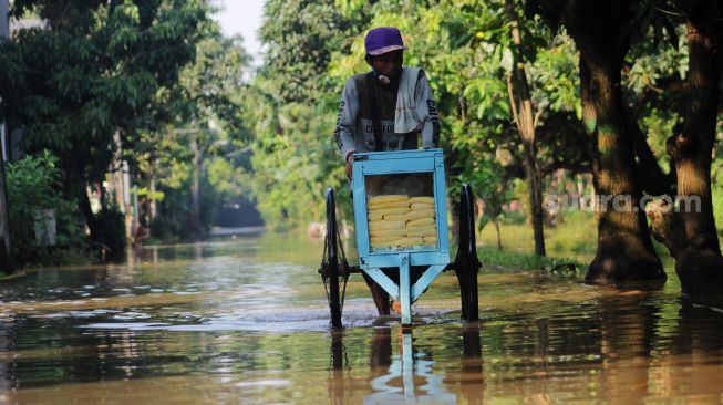 Warga melintas di genangan banjir Perumahan Bumi Nasio Indah, Bekasi, Kamis (15/4/2021). [Suara.com/Dian Latifah]