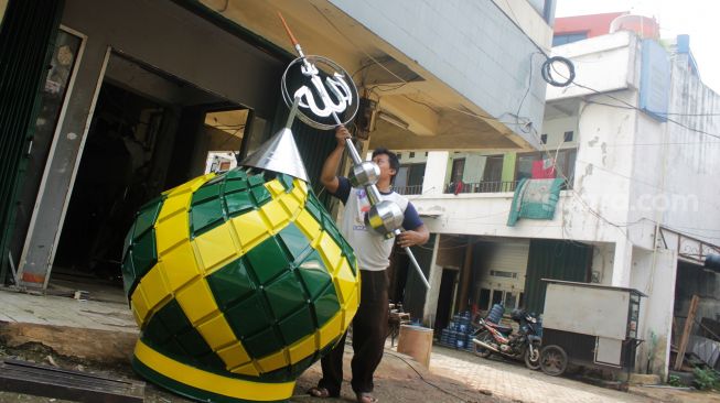 Pekerja menyelesaikan pembuatan kubah Masjdi dengan meletakkan tiang bertulis Allah di Kalimalang, Jakarta Timur, Jumat  (16/4/2021).[Suara.com/Dian Latifah]