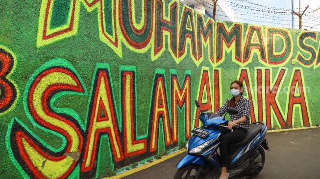 Warga melintas di depan mural bernuansa Islami di Gang Pelangi, Kalibata, Jakarta Selatan, Sabtu (17/4/2021). [Suara.com/Alfian Winanto]