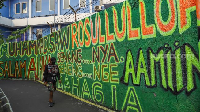 Warga berjalan di depan mural bernuansa Islami di Gang Pelangi, Kalibata, Jakarta Selatan, Sabtu (17/4/2021). [Suara.com/Alfian Winanto]