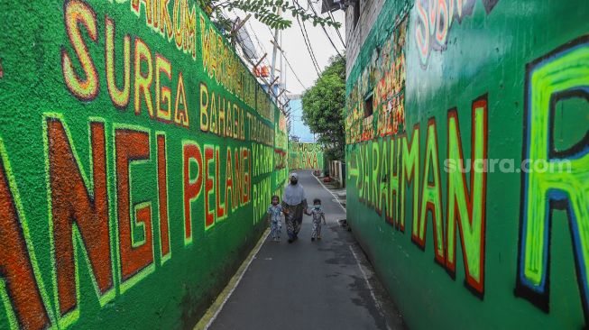 Warga berjalan diantara dinding dengan mural bernuansa Islami di Gang Pelangi, Kalibata, Jakarta Selatan, Sabtu (17/4/2021). [Suara.com/Alfian Winanto]