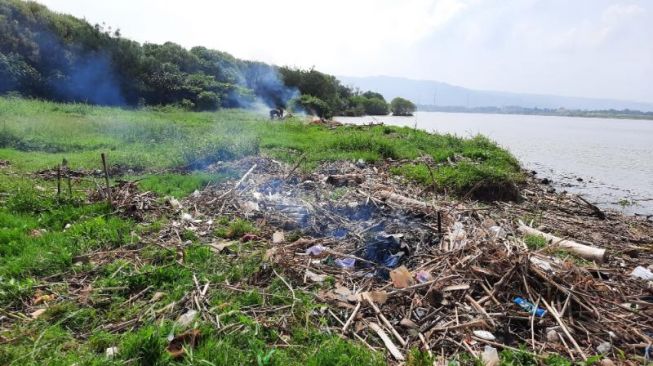 Warga membakar sejumlah sampah yang ada di sekitar tempat tambang pasir ilegal di Muara Sungai Opak, Bantul, Minggu (18/4/2021). [Muhammad Ilham Baktora / SuaraJogja.id]